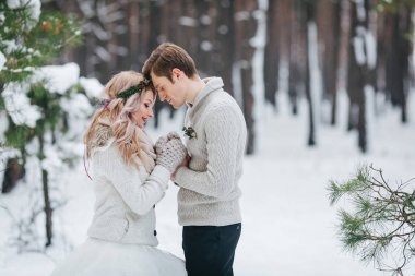 Neşeli gelin ve damat karlı ormandaki bej örme pullovers içinde. Yeni evliler alnına dokunuyor. Kış