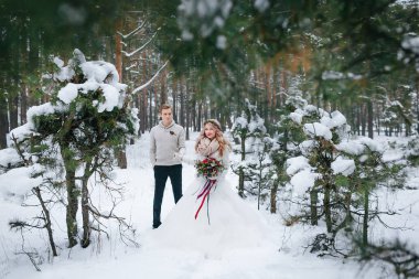 Güzel gelin damat bir buket ile karlı ormanda poz. Tam uzunlukta. Sanat
