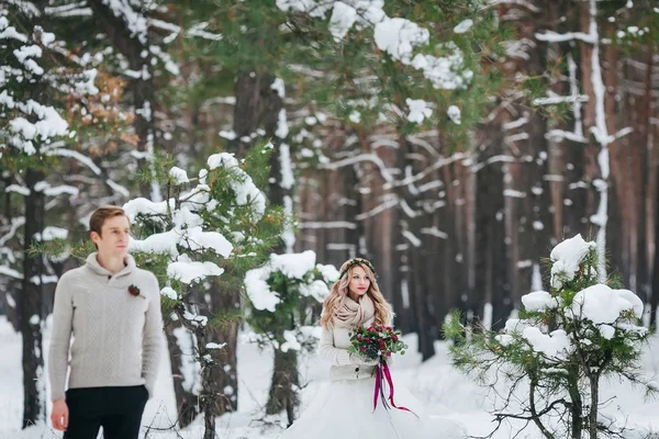 美丽的新娘与花束的背景下, 模糊的新郎在白雪皑皑的森林。冬季婚礼。艺术品. — 图库照片