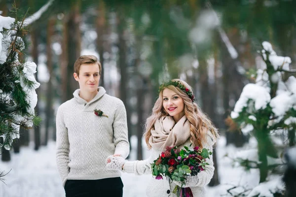 Fröhliche Braut und Bräutigam in beigen Strickpullovern spazieren durch den verschneiten Wald. selektiver Fokus auf Braut. Kunstwerk — Stockfoto