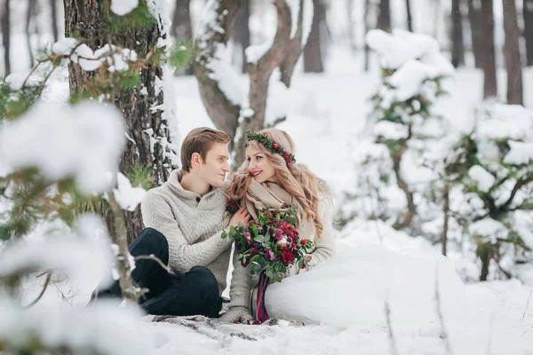 Los recién casados felices están sentados en un tartán en el bosque de invierno. La novia y el novio se miran. Boda de invierno —  Fotos de Stock