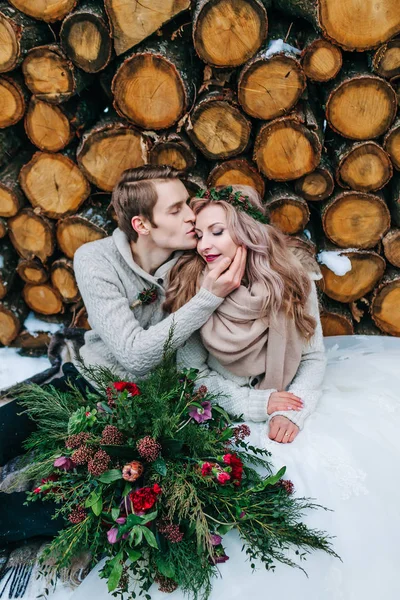 Mariée et marié se regardent tendrement. Les jeunes mariés élégants sont assis sur la neige sur le fond en bois. Mariage d'hiver — Photo