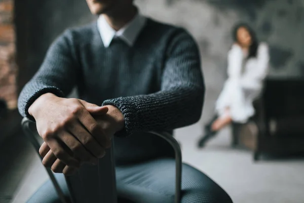 A man sits on the chair on a blurred background of his woman. Selective focus on the mans hands. Artwork — Stock Photo, Image