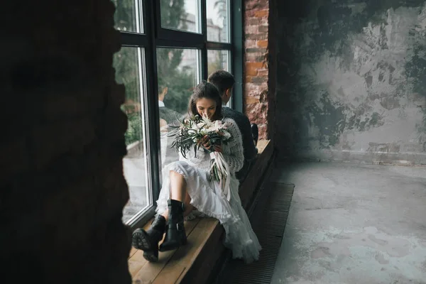 Cheerful bride with bouquet sits on the windowsill next to the groom. Artwork — Stock Photo, Image