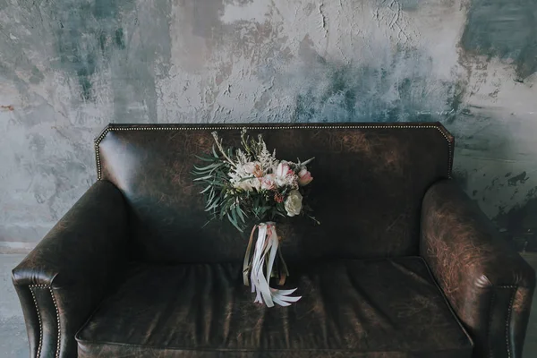 Rustikaler Hochzeitsstrauß mit hellen Rosen und anderen Blumen auf einem luxuriösen braunen Sofa. — Stockfoto