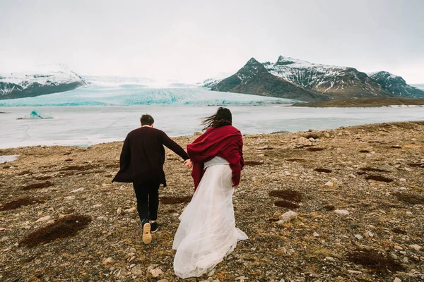 Noiva e noivo correm juntos. Islândia Casamento na Lagoa Glaciar. Visão traseira. Obra de arte — Fotografia de Stock