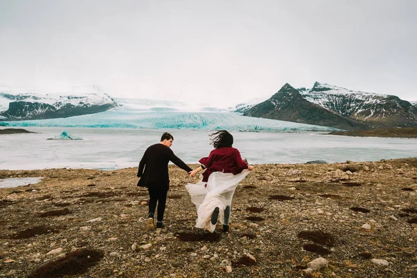 Bride and groom runs together. Iceland Wedding in Glacier Lagoon. Rear view. Artwork — Stock Photo, Image