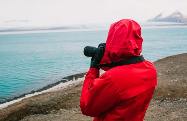Fotografo de viagens pela natureza, pessoa de casaco vermelho tirando fotos do rio na Islândia — Fotografia de Stock