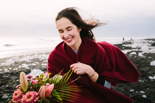 Χαρούμενη νύφη κάτω από καρό με ρουστίκ στην παραλία με μαύρη άμμο, Ισλανδία. Έργο τέχνης. Τα μαλλιά της κουνιέται από τον άνεμο — Φωτογραφία Αρχείου