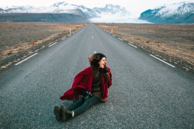 Yolda oturan ve güzel Dağları'nın arka planda çığlık neşeli genç kadın. İzlanda turistik. Rüzgarlı hava.