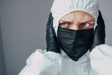 Siyah maskeli hemşire başını tutup sol tarafa bakıyor ve Coronavirus salgınını nasıl durduracağını merak ediyor. Bunun tehlikelerini ve sonuçlarını düşünüyor.. 