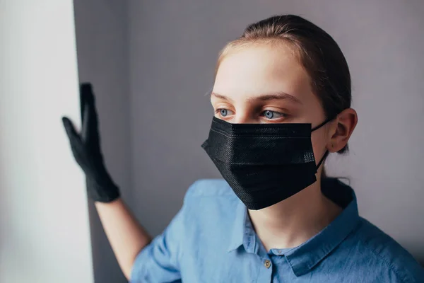 Siyah maskeli ve tıbbi eldivenli bir hemşire başka yere bakar ve insanları koronavirüsten nasıl koruyacağını düşünür. Klinikteki doktor virüs salgınını nasıl durduracağını düşünüyor..