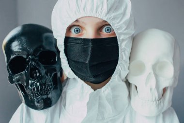 Viral koruyucu giysili bir akciğer bilimci, omuzlarında beyaz ve siyah kafatasları olan tıbbi bir maske kameraya şok edici bir bakış. Kimin yaşayıp kimin öleceğine koronavirüslü hastalar karar verir.