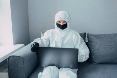 Viral koruyucu giysili ve siyah maskeli bir hemşire dizüstü bilgisayarda çalışıyor ve virüs salgını hakkında bilgi topluyor. Koronavirüs salgını yüzünden karantinaya alındı.. 