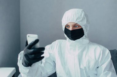 Siyah maskeli ve tıbbi eldivenli bir doktor video görüşmesinde arkadaşlarıyla konuşuyor çünkü koronavirüs salgınının yayılması nedeniyle virüs uzmanı karantinada..