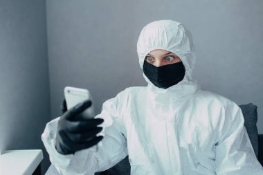 Viral koruyucu giysili, ilaç maskeli ve siyah eldivenli bir hemşire telefona bakar ve virüsün yayılması konusunda endişelerini karantinaya alır. Virolog koronavirüs salgınından korkuyor..