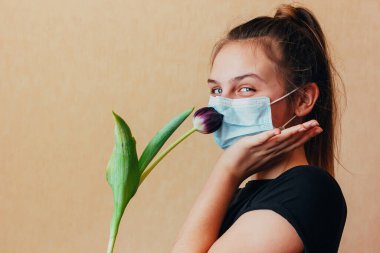 A young girl in a mask holds a purple tulip in her hands and tries to smell the fragrance through the barrier. Cannot enjoy life due to quarantine restrictions due to outbreaks of coronavirus clipart