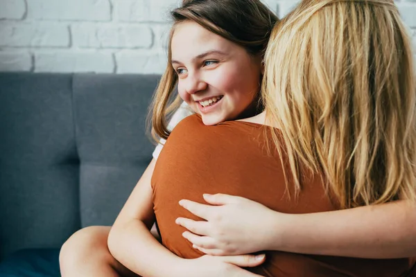 people and family concept - happy smiling girl with mother hugging on sofa at home.Happy mother\'s day! Mom and her daughter child girl are hug. Family holiday and togetherness