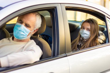 granddaughter sitting behind and looking through window at camera. Senior man driving car.  Grandfather and granddaughter in face mask be safe in the car. Road safety. Coronavirus pandemic. clipart
