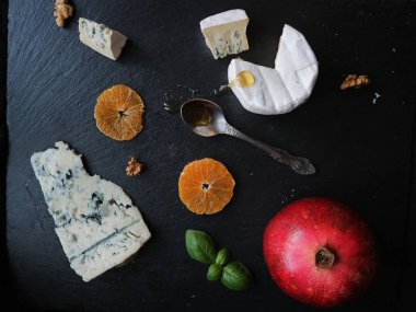 Çeşit çeşit peynir, meyve, taze meyve ile siyah bir taş tabloda tatlım. Gorgonzola, Brie, rokfor peynir mavi. Çeşitli aperatifler ve mezeler. Üstten Görünüm. Gurme mutfağı. Lezzetli yemekler.