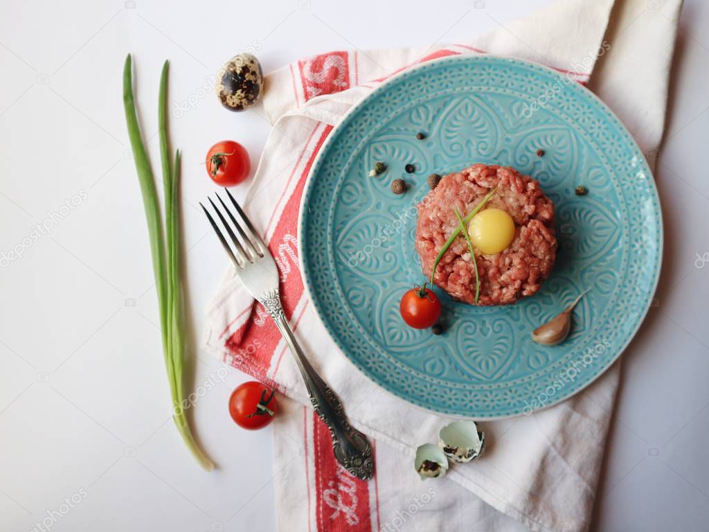 Minced meat with quail egg, fresh spring onion, spices, cherry tomatoes, garlic. White wooden background. Raw ingredients ready for cooking. Closeup. Space for text. Delicious tartar.