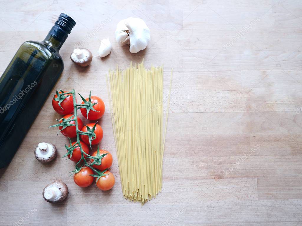 Italian cuisine concept. Pasta spaghetti, fresh cherry tomatoes, button champignons, olive oil, garlic. Healthy simple eating. Traditional food on a wooden background.