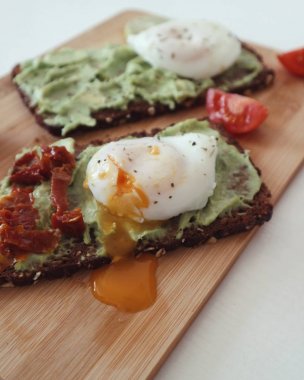 Ahşap bir gemide kuru domates ile lezzetli haşlanmış yumurta avokado tost. Temiz gıda sağlıklı beslenme kavramı. Yakın çekim.