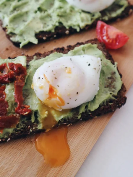 Delicious poached egg on avocado toast with dry tomatoes on a wooden board. Healthy clean food eating concept. Close up.