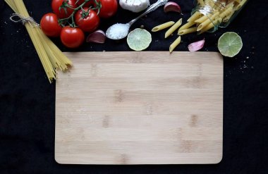 wooden cutting board and raw ingredients for cooking: pasta, cherry tomatoes, garlic, lime, salt. Food background with copy space. Flat lay