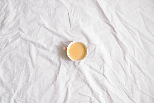 Cup of coffee on white cotton sheet. Flat lay, top view