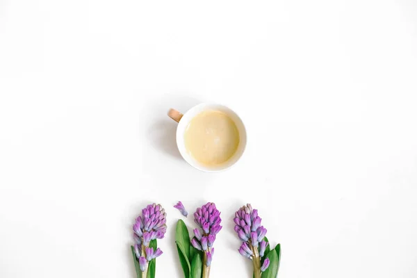 Lilac hyacinth flowers and coffee cup on white background. Flat lay, top view