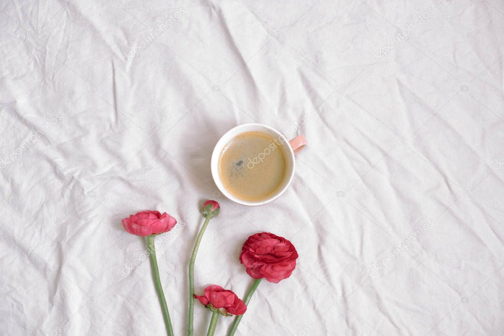 Cup of coffee and pink anemone flowers on cotton sheet. Flat lay, top view, copy space