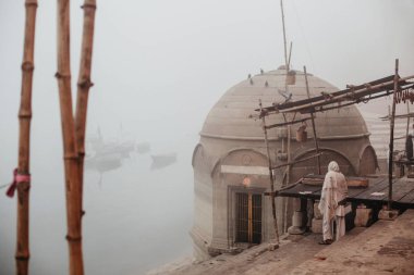 Figure on ghat near Ganges river in fog. Varanasi, Banaras, India clipart