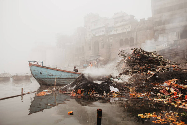 Quay with ghats and boats and funeral fires in Varanasi. River Ganges