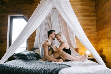 Evde güzel çift birlikte. Güzel kadın ve çekici adam bir yatak üzerinde oturan ve sarılma ev Giyim Giyim Eşyası.