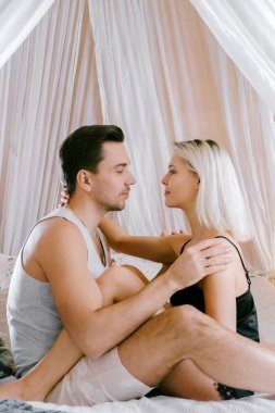 Evde güzel çift birlikte. Güzel kadın ve çekici adam bir yatak üzerinde oturan ve sarılma ev Giyim Giyim Eşyası.