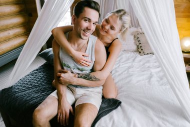 Evde güzel çift birlikte. Güzel kadın ve çekici adam bir yatak üzerinde oturan ve sarılma ev Giyim Giyim Eşyası.