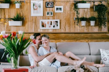 Evde güzel çift birlikte. Güzel bir kadın ve bir kanepe sarılma üzerinde oturan çekici adam şık rahat kıyafetler