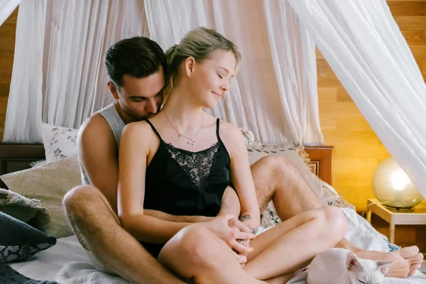 Evde güzel çift birlikte. Güzel kadın ve çekici adam bir yatak üzerinde oturan ve sarılma ev Giyim Giyim Eşyası.