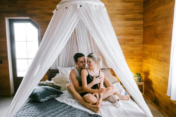 家で一緒に素敵なカップルです きれいな女性とベッドの上に座って 抱いて家の服服を着て魅力的な男性 — ストック写真