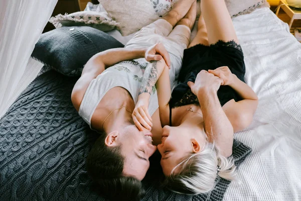 家で一緒に素敵なカップルです きれいな女性とベッドの上で横になっている キスしてハグ家の服を着て魅力的な男性 — ストック写真