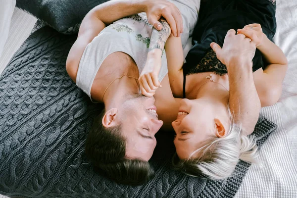 家で一緒に素敵なカップルです きれいな女性とベッドの上で横になっている キスしてハグ家の服を着て魅力的な男性 — ストック写真