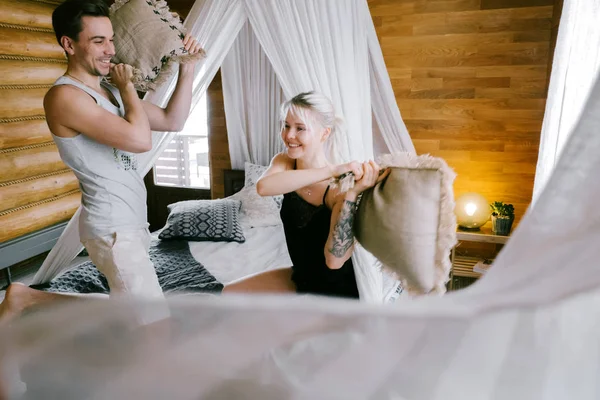 Evde güzel çift birlikte. Güzel kadın ve çekici adam bir yatak üzerinde oturan ve yastık ile mücadele ev Giyim Giyim Eşyası