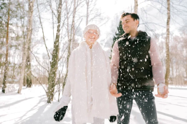 Güzel çift birlikte kar ile oynarken açık havada güneşli bir günde. Güzel kadın ve çekici adam gülüyor ve birbirlerine gülümseyen şık rahat kıyafetler giymiş.