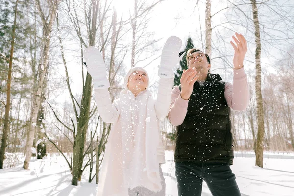 Güzel çift birlikte kar ile oynarken açık havada güneşli bir günde. Güzel kadın ve çekici adam gülüyor ve birbirlerine gülümseyen şık rahat kıyafetler giymiş.