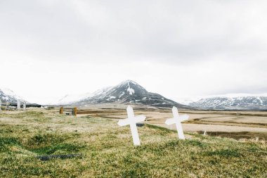 İzlanda mezarlıkta iki çapraz mezar işaretleri ve arka planda dramatik karla kaplı dağlar