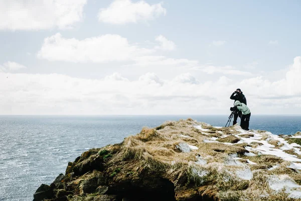 Two photographers taking pictures on a cliff against the ocean. Latrabjarg, Iceland. Travel photographer concept