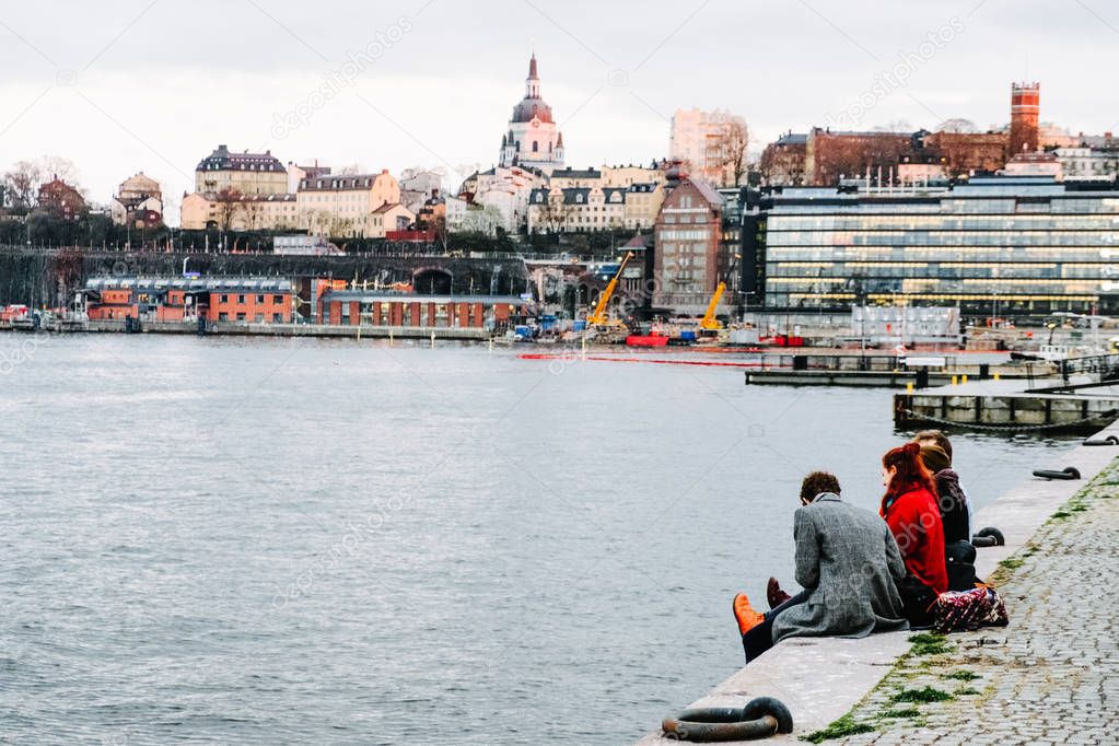 People relaxing on embankment near Gamla Stan, Stockholm old town. Lake Malaren