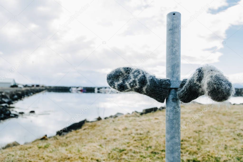 Icelandic handcraft woolen mittens with pattern on a pillar near a lake 