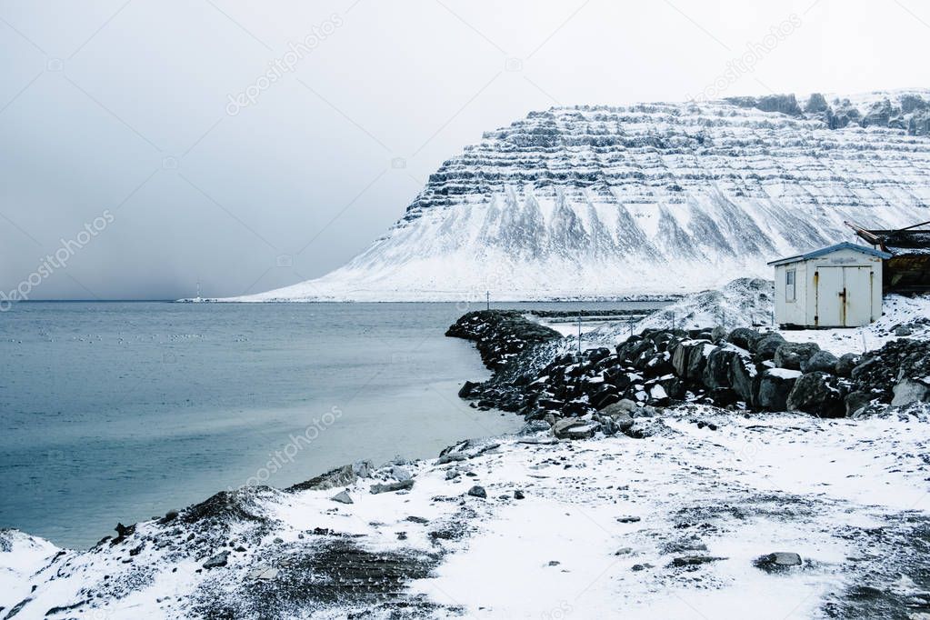 Lonely abandoned house at snowy coastline with fjord in West Iceland. Winter northern scenery